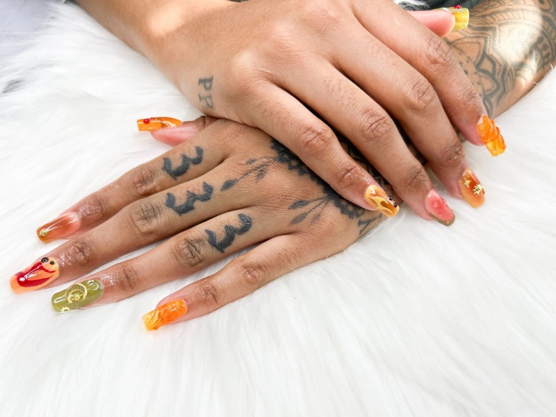 Long orange ombre nail set with gold charms by TLC Nails and Esthetics in Nottingham, MD